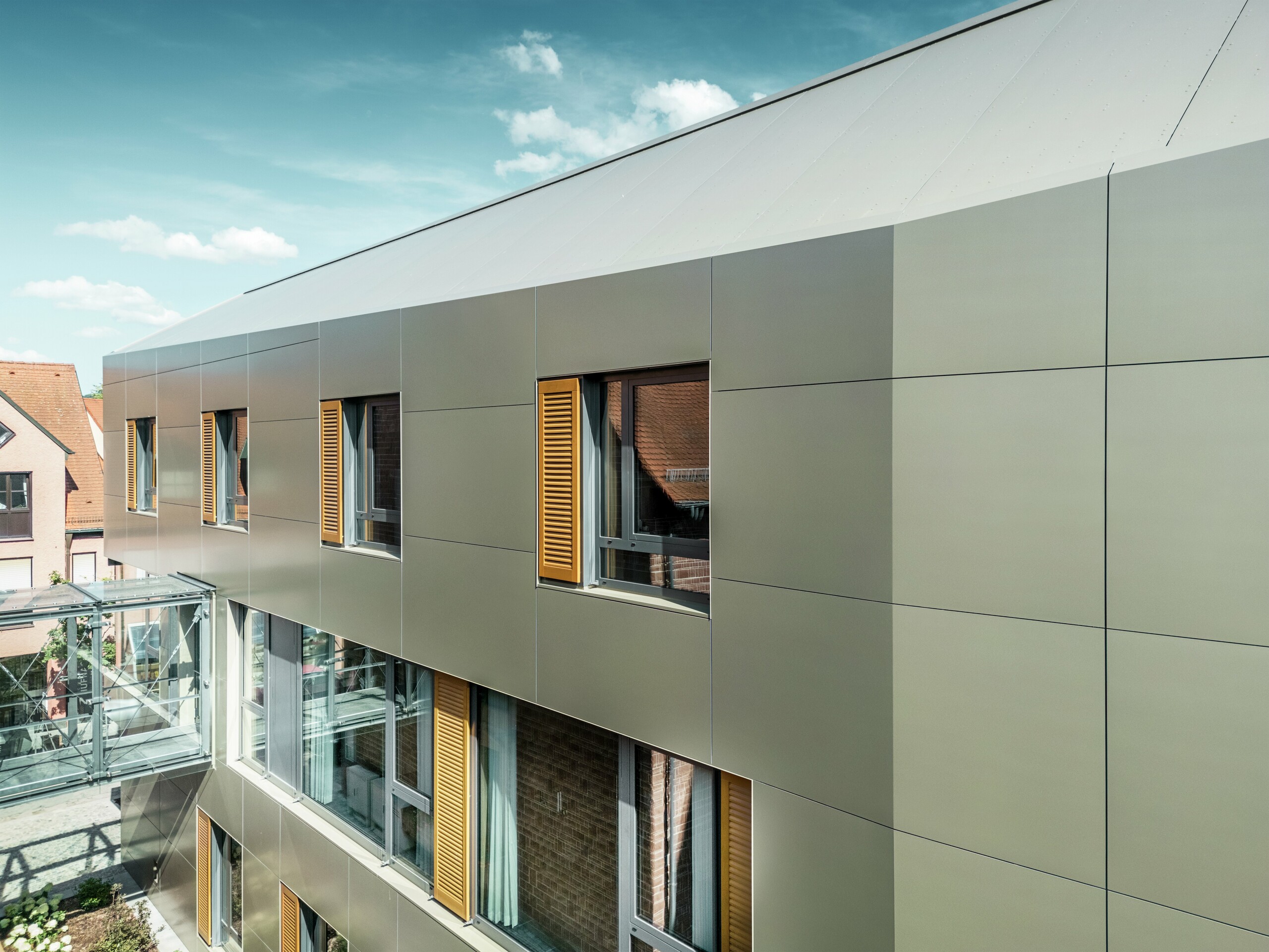 The image shows a section of the façade of the town hall in Alzenau, Germany, featuring bronze aluminium composite panels from PREFA. The panels are laid in a modern rectangular pattern.