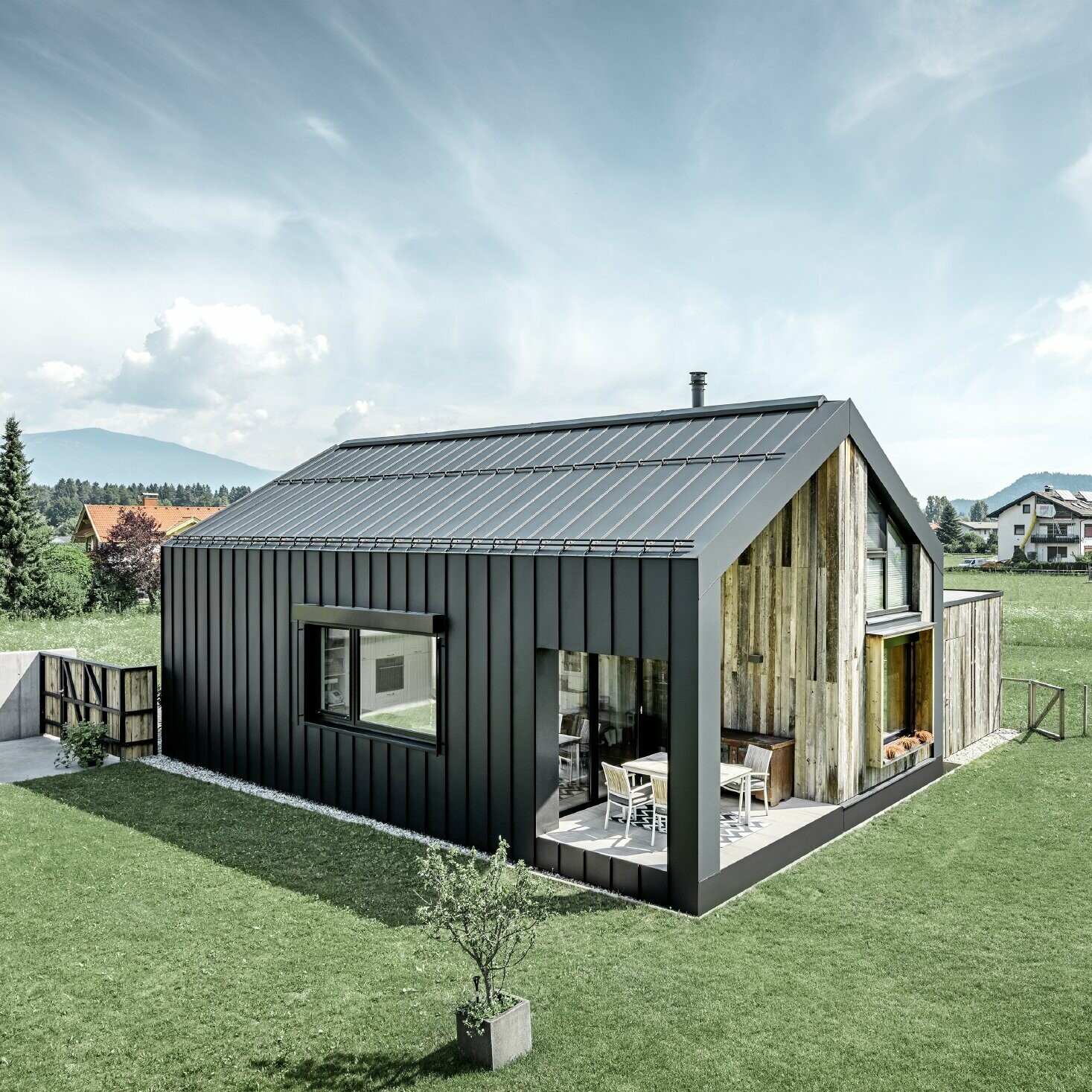 Detached house with gable roof, roof and façade are covered with PREFALZ standing seam from PREFA in P.10 anthracite. The panels of the roof surface extend across the façade. Part of the façade is clad with weathered wood.