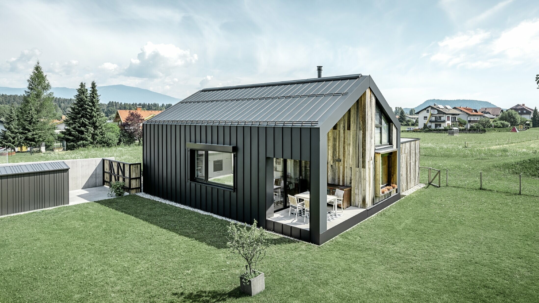 Detached house with gable roof, roof and façade are covered with PREFALZ standing seam from PREFA in P.10 anthracite. The panels of the roof surface extend across the façade. Part of the façade is clad with weathered wood.