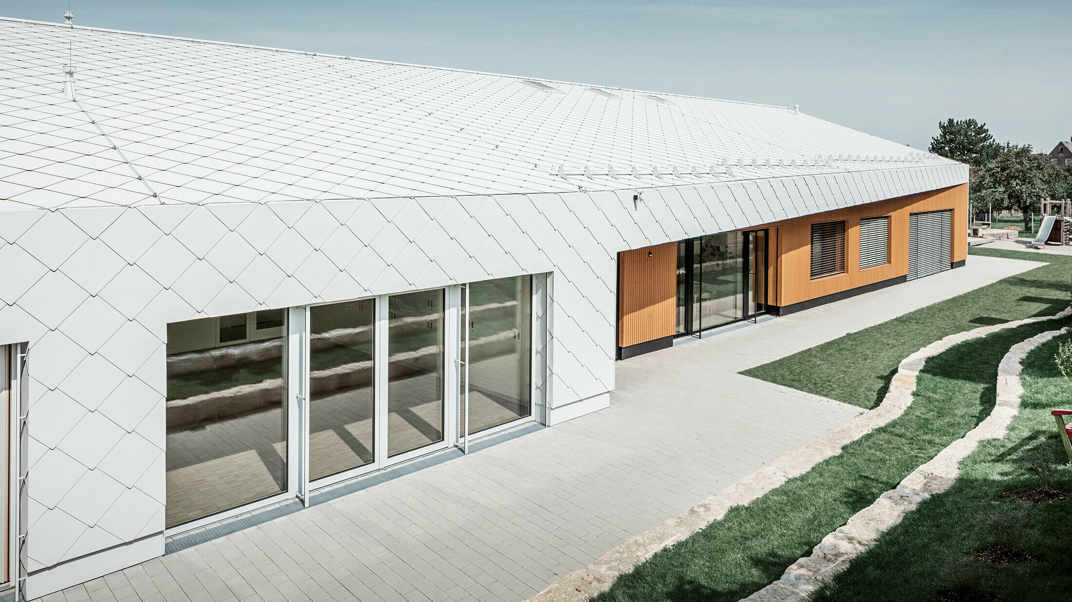 Nursery with the PREFA roof and façade tiles 44 in Prefa white, the roof surface extends over the façade; large window areas