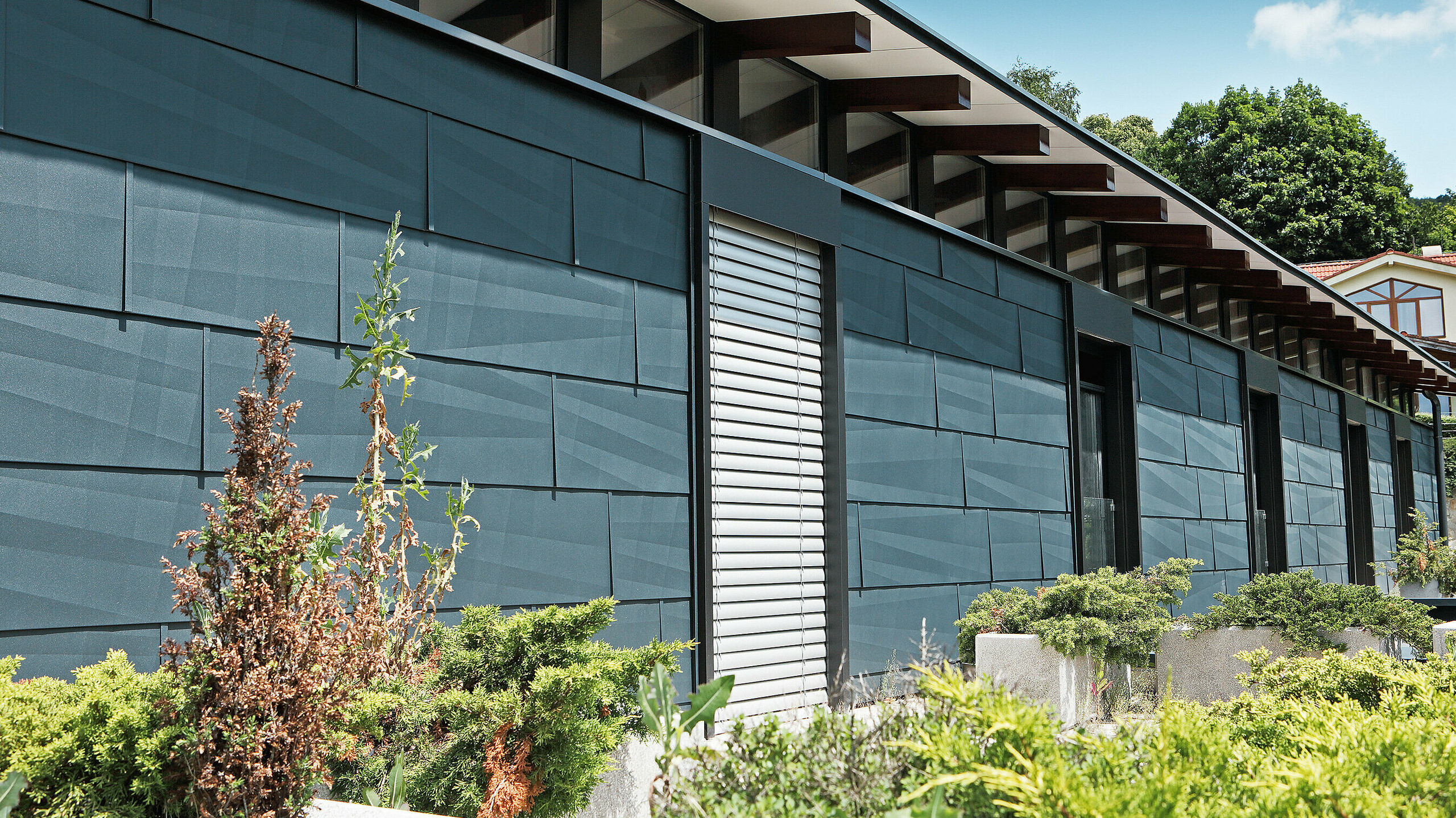 Modern exposed building side designed using FX.12 façade panelling in anthracite, with a garden.