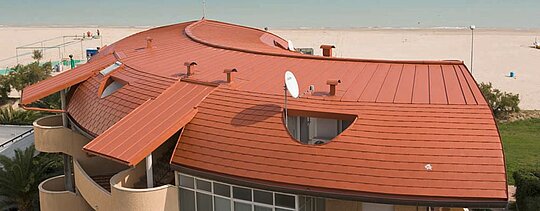 Rounded roof in residential complex, covered with PREFA roof shingles and standing seam roof - PREFALZ from PREFA in brick red.