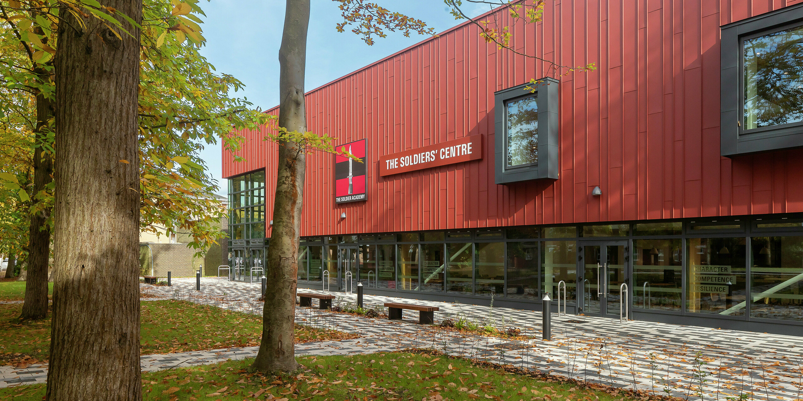 A detailed view of the modern facade elements at the Soldiers' Centre in Pirbright: the precisely installed standing seam cladding made of PREFALZ in P.10 oxide red, which sets a visual accent in combination with the striking window frames in P.10 anthracite. The fine lines and shadows emphasise the high-quality workmanship and innovative design of PREFA aluminium products – proof of sustainable and contemporary architecture.