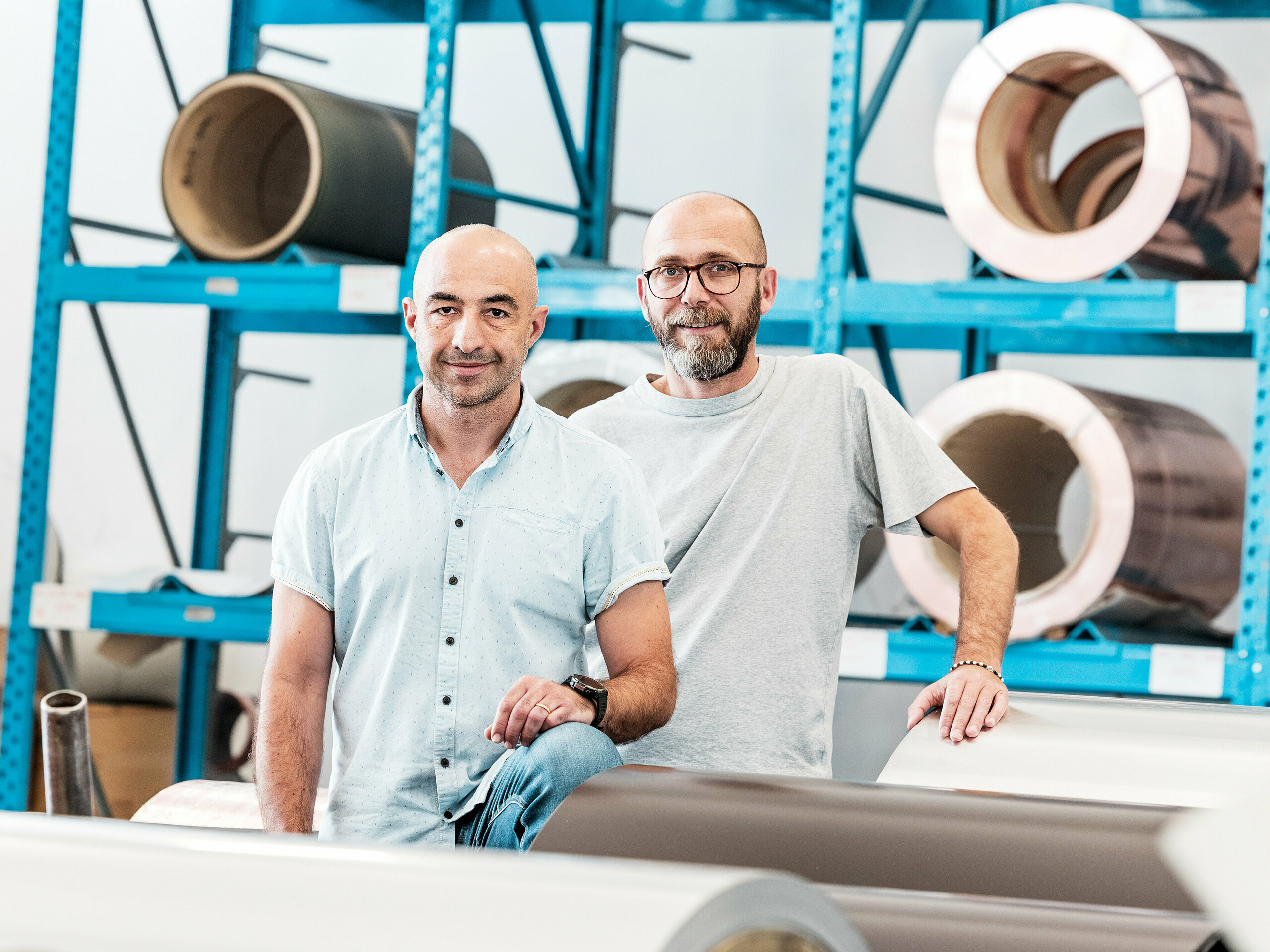 Zwei Handwerker in einer Aluminiumhalle vor aufgewickelten Metallspulen – ein modernes Arbeitsumfeld für Aluminium-Dach- und Fassadensysteme.