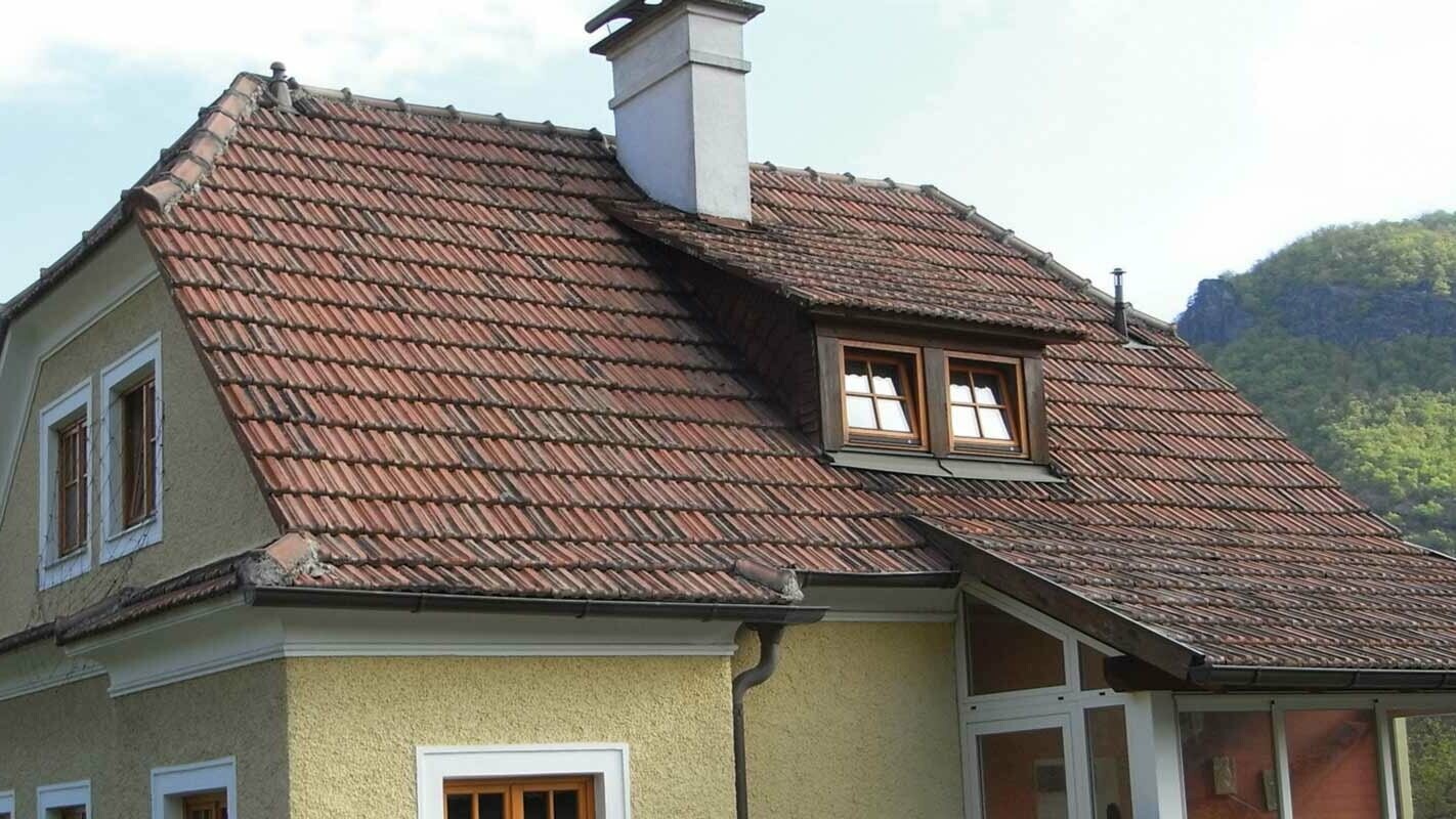 Old detached house with a tiled roof and a rough, yellow rendered façade before roof renovation