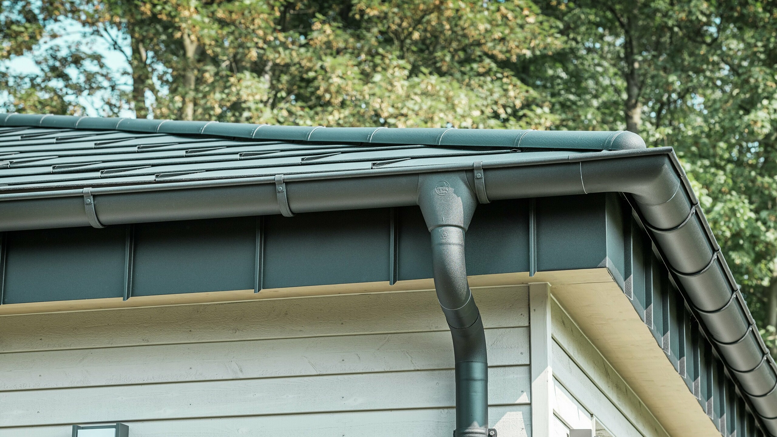 Detailed view of PREFA roof drainage on a bungalow in Rommerskirchen. The high-quality on-roof gutter and downpipe in P.10 black ensure reliable roof drainage when it rains. The durable PREFA aluminium products combine functionality with modern, elegant design.