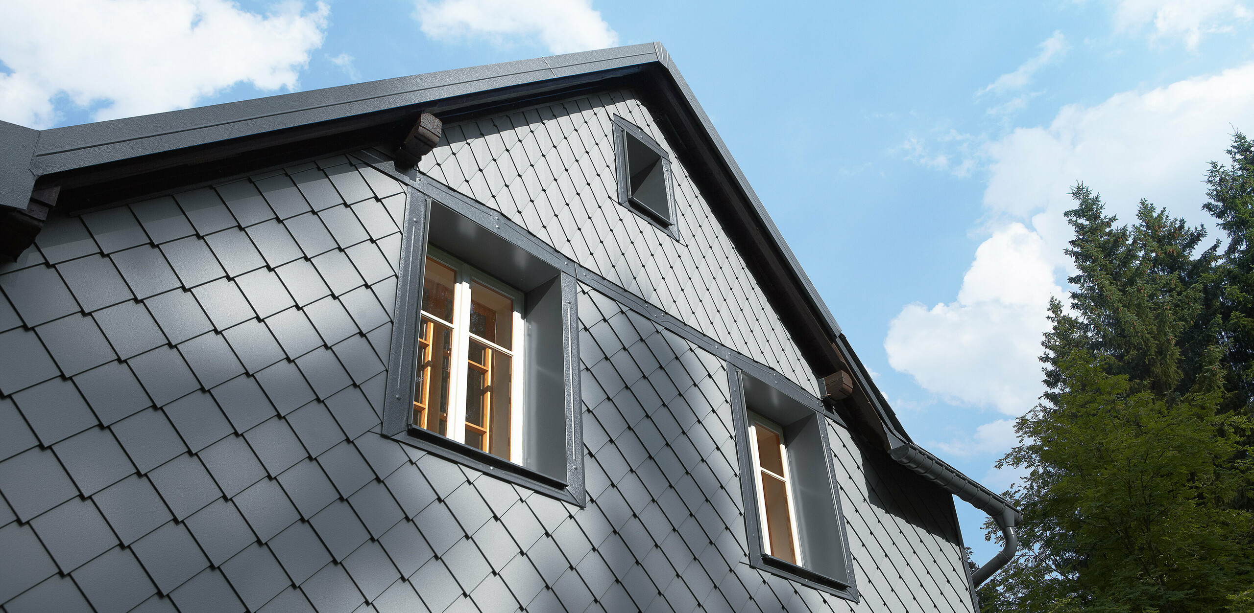 The side of a building that faces the direction of the prevailing weather clad with PREFA’s rhomboid façade tile 20 × 20 and small-format rhomboid tile on the façade