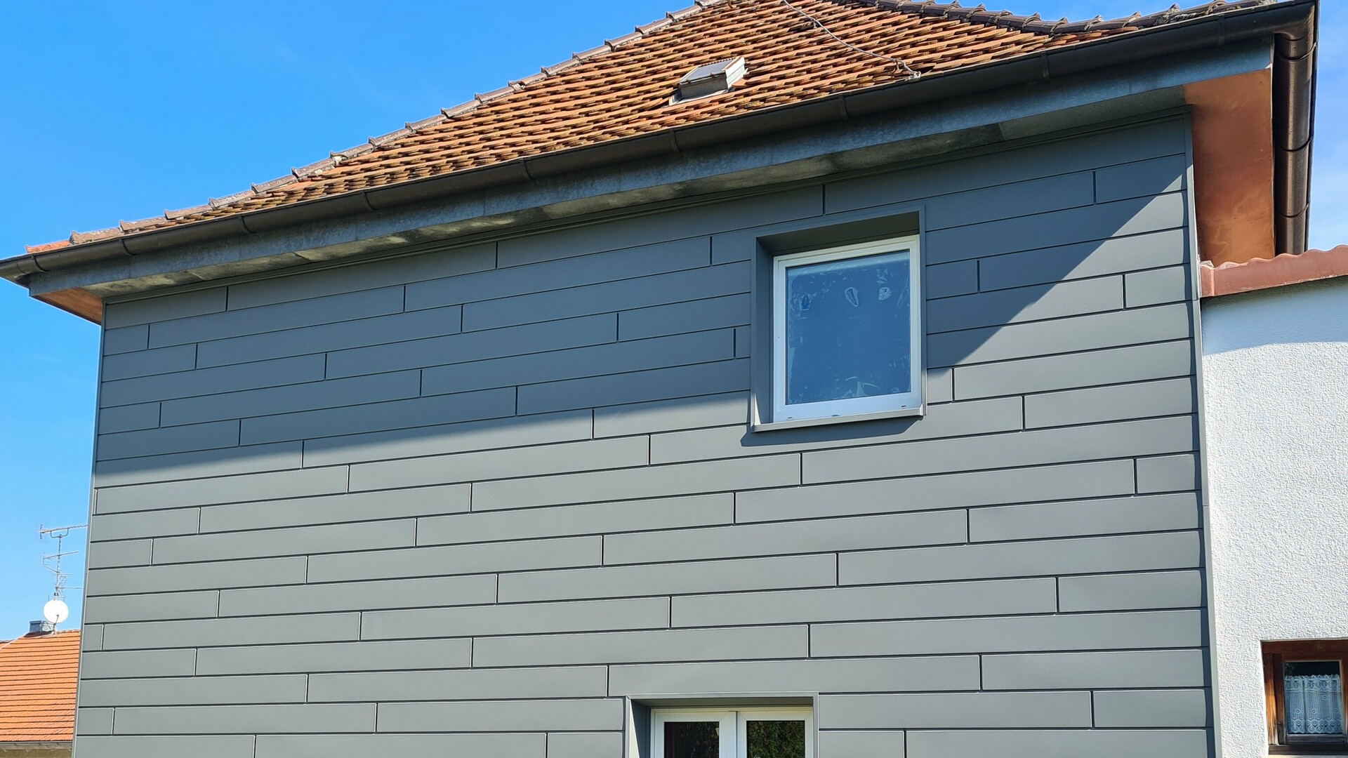 Einfamilienhaus in Deutschland mit Fassadensanierung. Produkt: PREFA Siding P.10 Hellgrau. Material Sockelverkleidung: PREFABOND P.10 Dunkelgrau. Material Fassade: Siding 200x1,0mm mit Schattenfuge Länge 2200mm. Verlegeart: "Wilder Verband".
