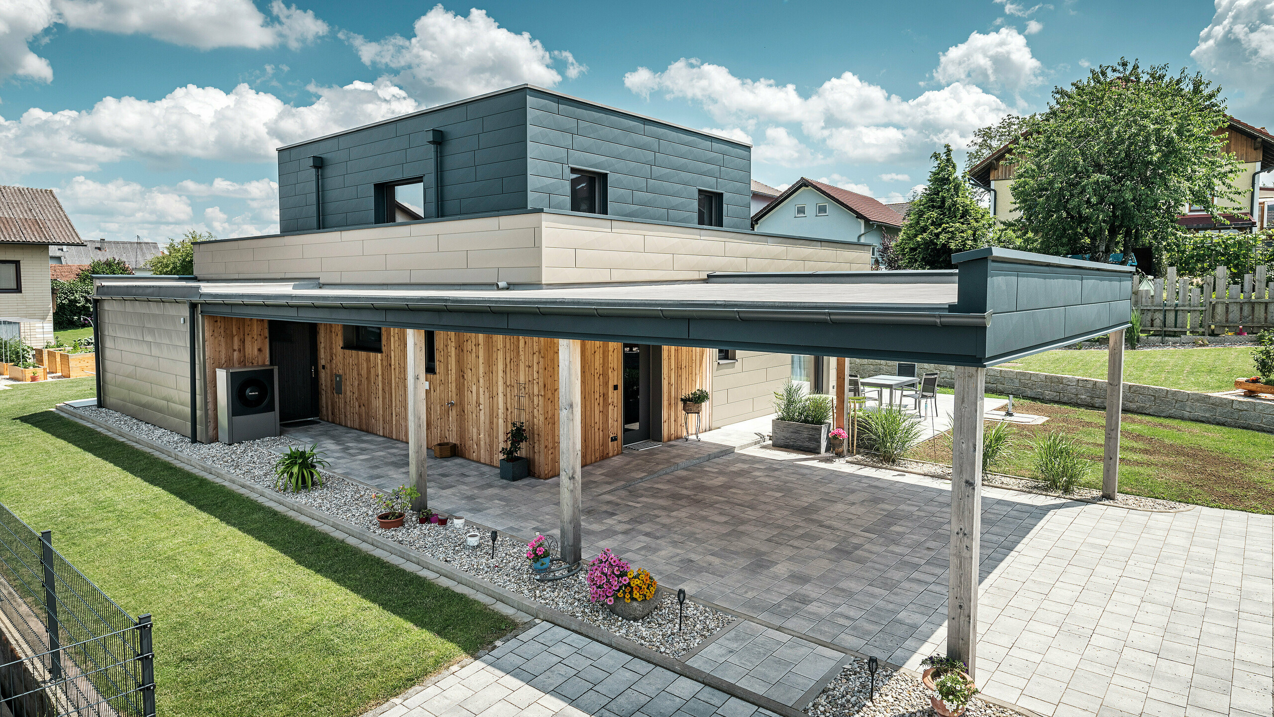 Aerial view of the driveway of a modern detached house in Wippenham, Austria, with a two-tone PREFA aluminium façade in bronze and anthracite. The house showcases the stylish integration of Siding.X façade panels and wood cladding. The covered carport is clearly visible and seamlessly integrated into the architecture of the house. The well-kept garden and terrace area emphasise the modern and functional design of the building.