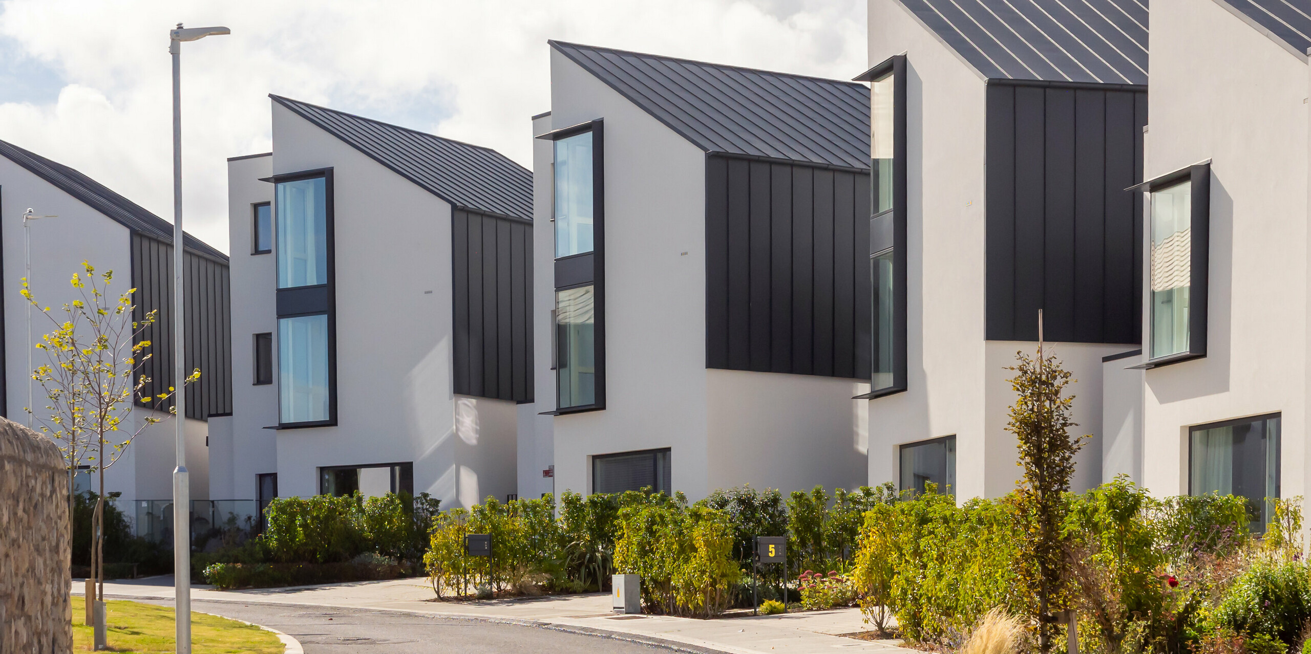 Modern terraced housing development Watson Place near Dublin with clear, asymmetrical roof shapes and dark PREFALZ standing seam cladding in P.10 anthracite. The large windows and striking aluminium surfaces emphasise the dynamic architecture. The durable PREFA products offer reliable weather protection and give the residential complex an elegant, high-quality appearance.