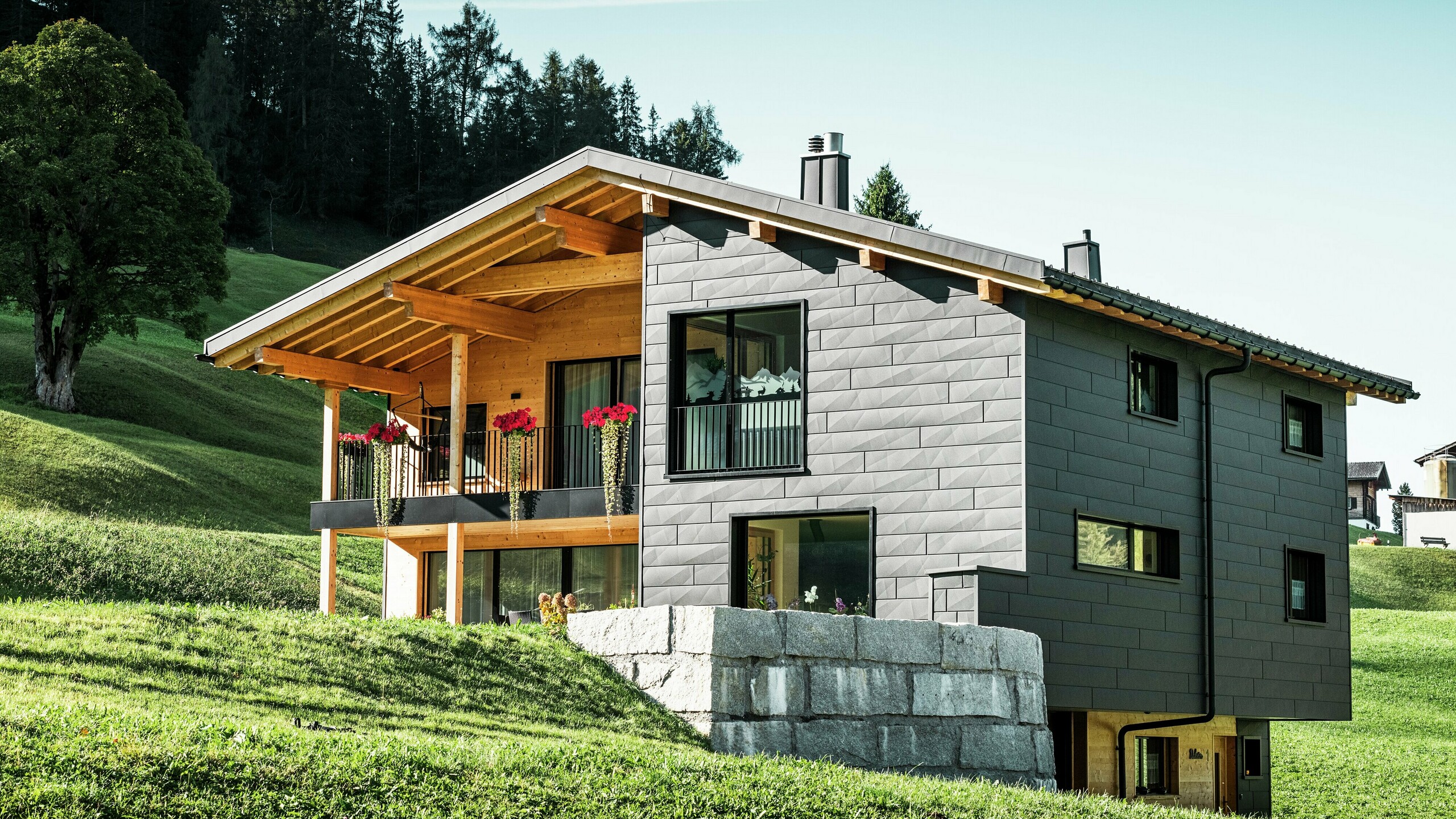 Dieses moderne Einfamilienhaus in Ascharina, Schweiz, fügt sich harmonisch in die grüne Alpenlandschaft ein. Das Gebäude ist komplett mit den langlebigen und witterungsbeständigen PREFA Siding.X Fassadenpaneelen in P.10 Schwarz verkleidet, die dem Bauwerk ein einzigartiges Erscheinungsbild verleihen. Der Holzbalkon ergänzt die dunkle Aluminiumhülle perfekt und setzt einen natürlichen Akzent.