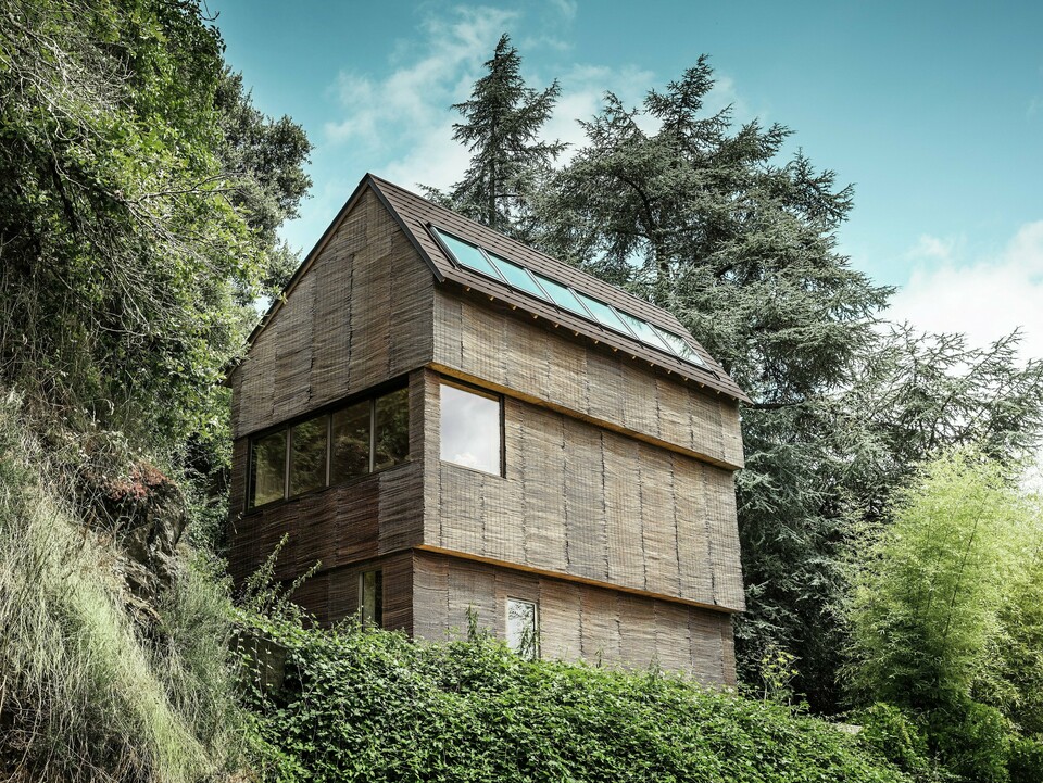 Ein Haus im Westen Frankreichs mit PREFA-Dachschindeln in der Farbe P.10 Walnussbraun, gelegen an einem steilen Hang – ein modernes Design mit einer Fassade aus Weidenholz und einem energieeffizienten Dach.