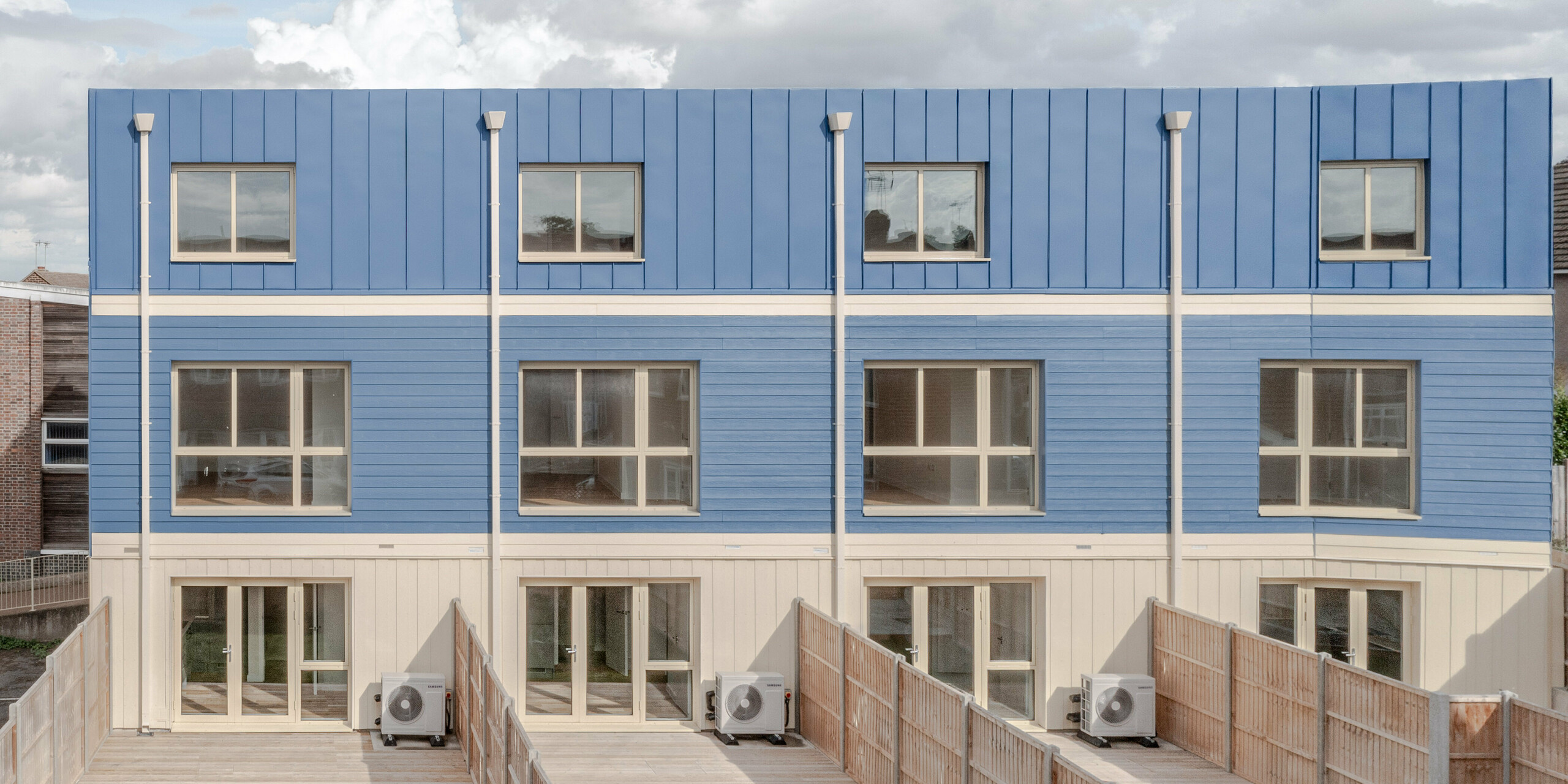 The garden side of the terraced houses in Goldsmith Mews features the striking dusty blue FALZONAL standing seam façade and roof design, which gives the buildings a clear, modern character. The precise vertical folds and blue panels create a rhythmic, lively façade. The bright ground floor areas and large windows open up the architecture to the external environment. The high-quality PREFA aluminium offers lasting weather protection, high colour and shape stability, and enables a durable, aesthetic design with high recognition value.