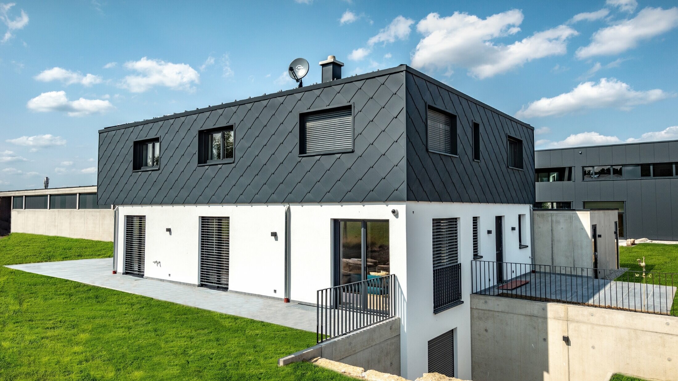 Modest new build with flat roof; the ground floor has a white plaster finish while the upper floor is clad in the large PREFA rhomboid façade tile in anthracite.