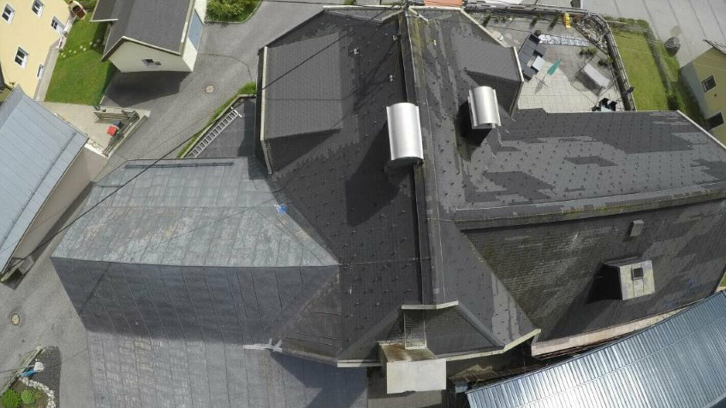 Aerial view of an old roof with many details – channels, dormers and chimneys. The old roof has been repaired multiple times and is stained.