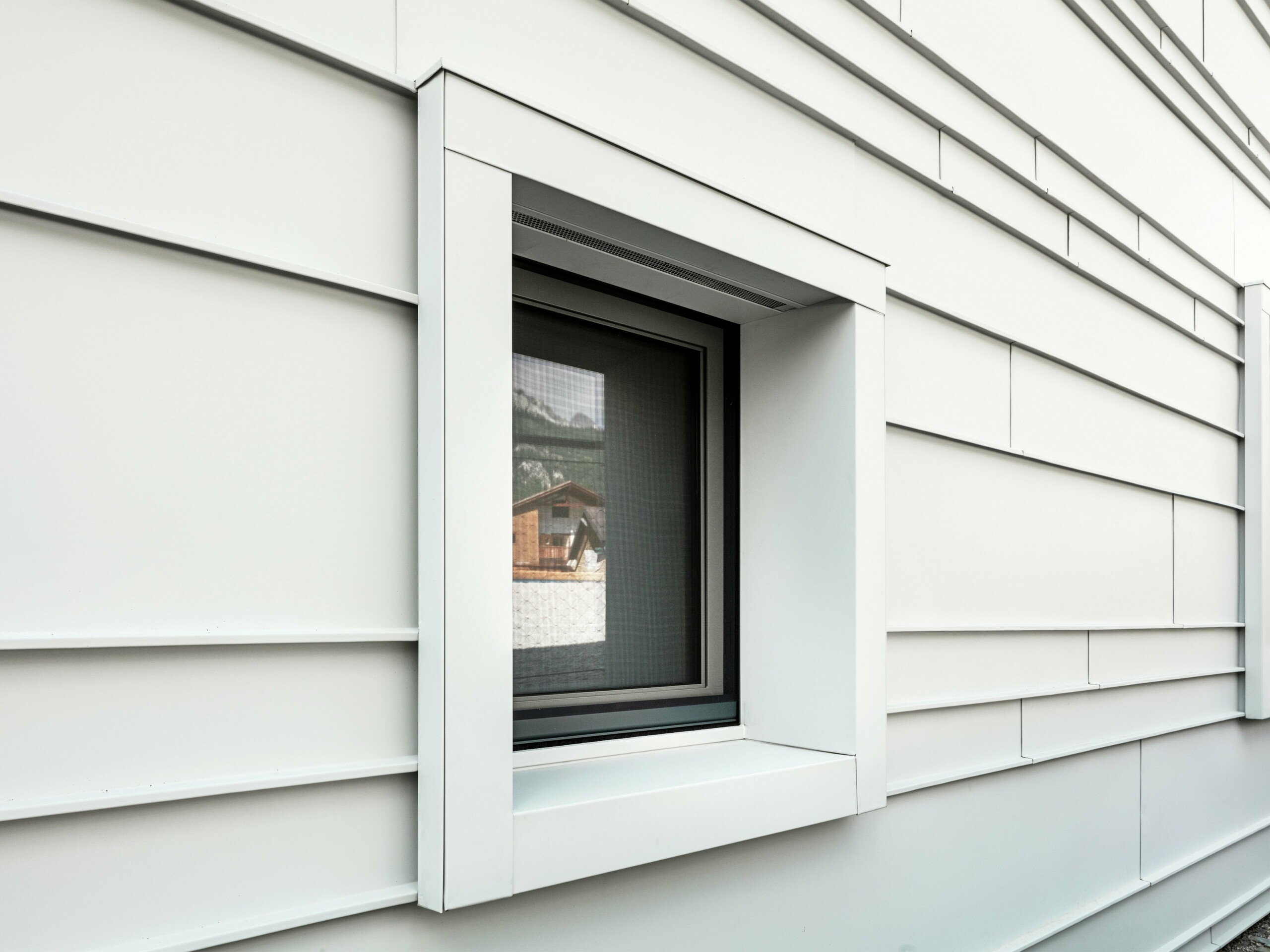 Detailed view of a striking window section in a rear-ventilated façade made of PREFALZ P.10 in PREFA white. The horizontally laid aluminium panels provide structure, clarity and a modern aesthetic. The strikingly prominent window frames of the ‘Tempesti’ barracks always begin and end exactly at a fold line. This deliberately emphasises the structure of the aluminium.