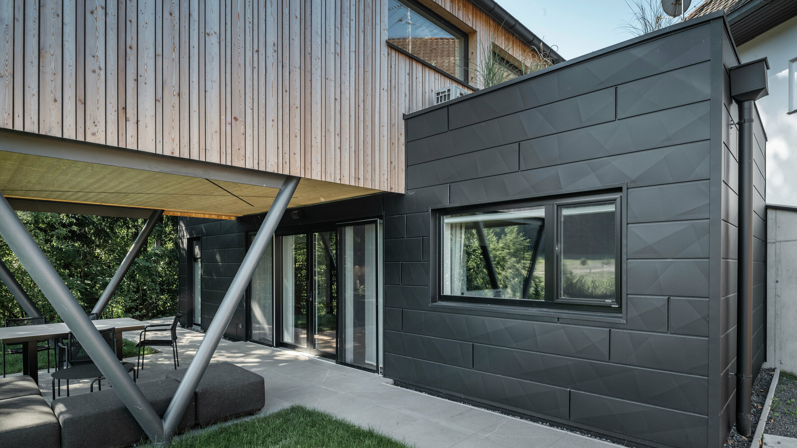 Architectural highlight: “Woodstock Chalet 5” in St. Martin am Innkreis, Upper Austria. The modern wedding venue is accentuated by the use of anthracite-coloured PREFA Siding.X façade panels. The aluminium elements form a striking contrast to the light-coloured wood panels and the metallic support structures. The dark window frames blend harmoniously into the façade design, giving the building an elegant appearance. This image shows the aesthetic balance between natural wood texture and the industrial charm of the aluminium façade, which is representative of contemporary building design.