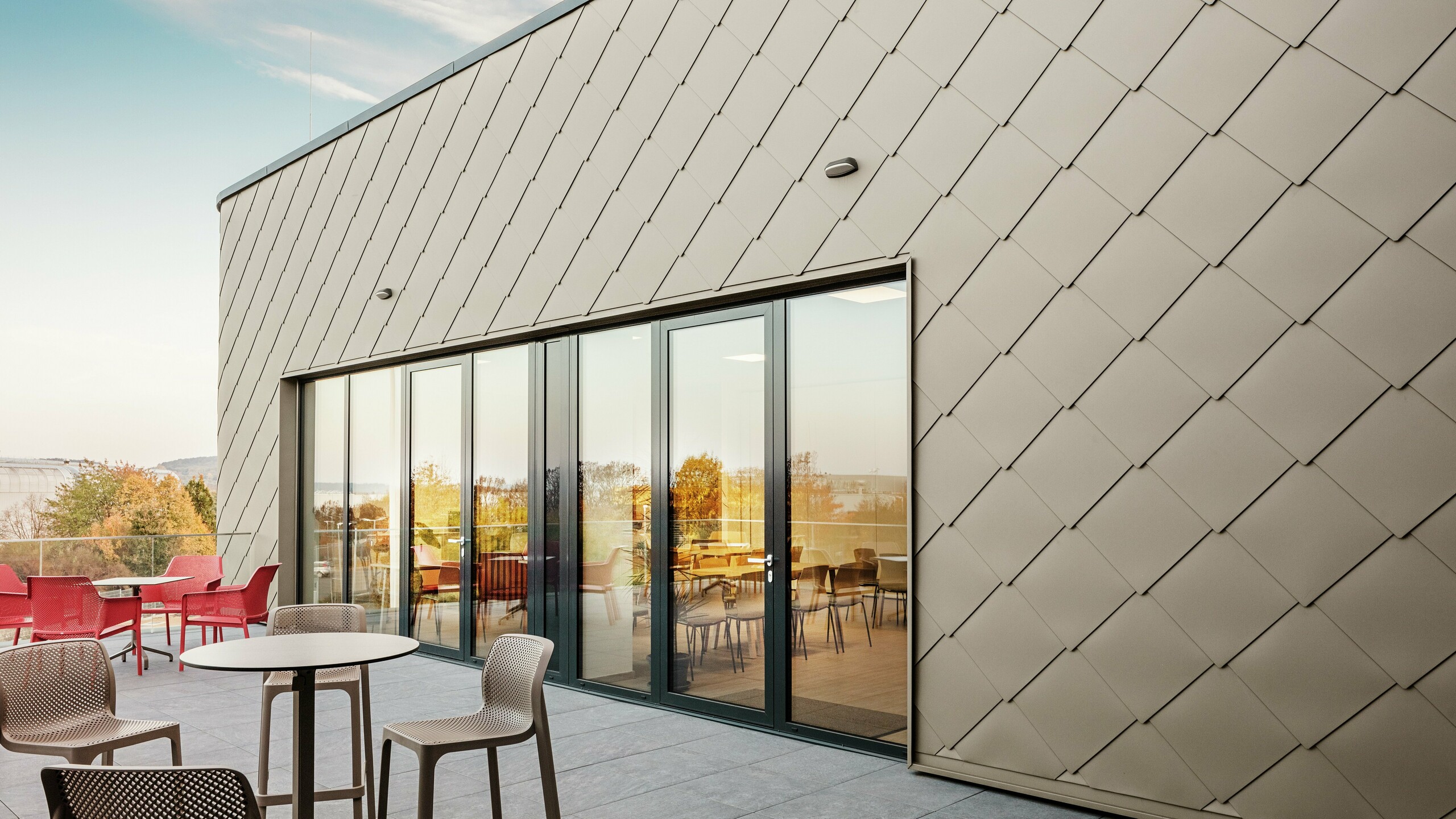 The façade of the new PREFA site in Törökbálint impresses with its elegant PREFA rhomboid façade tiles 44 × 44 in P.10 Prefabronze. The precisely installed aluminium façade ensures a modern, dynamic appearance while offering maximum protection against the elements. The generous glass front connects the internal and external areas and creates a bright and inviting atmosphere on the spacious terrace.