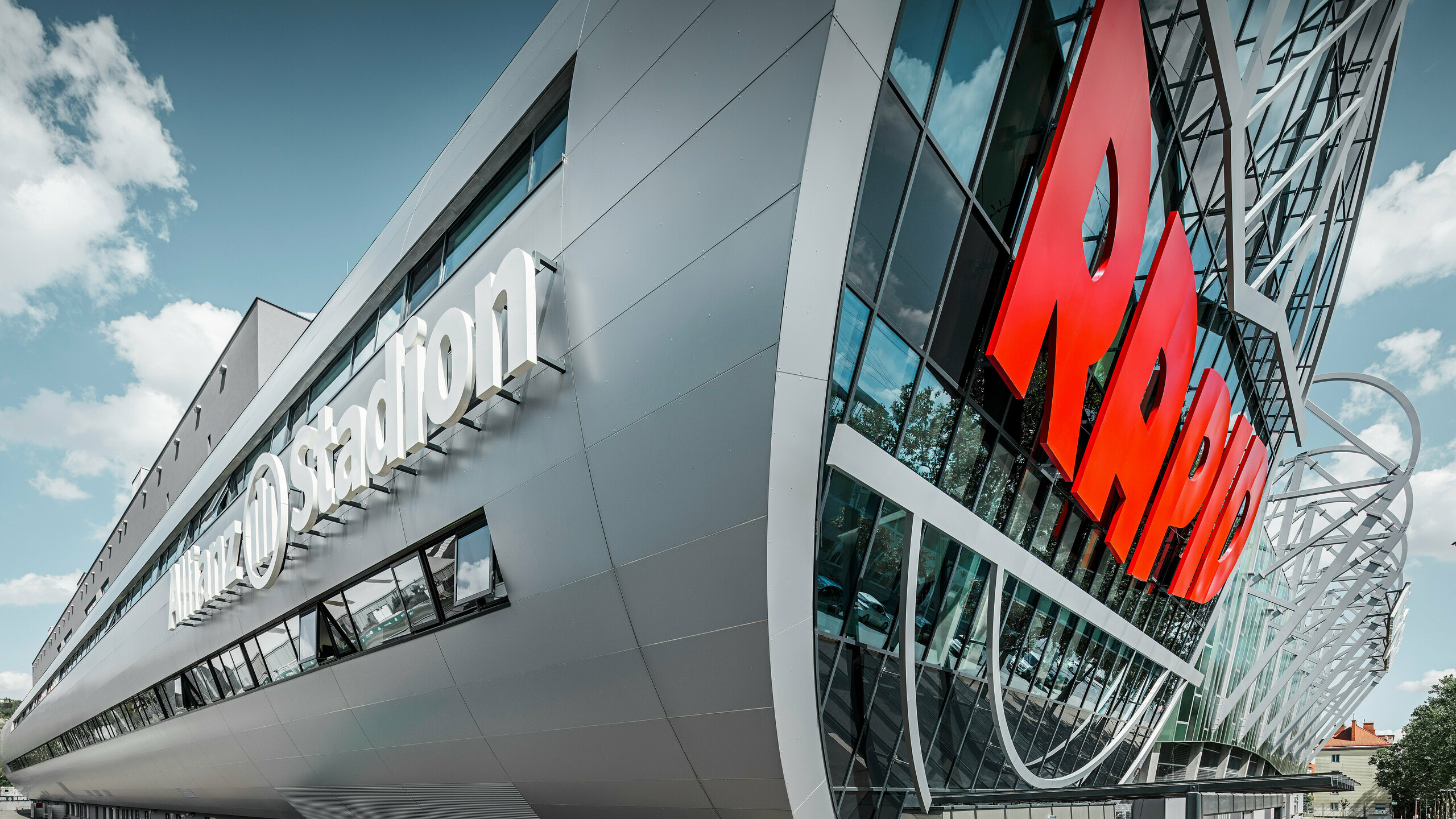 Nahaufnahme der Fassade des Allianz Stadions, Heimat des SK Rapid Wien. Die eindrucksvolle Röhre im Eingangsbereich präsentiert die PREFA Aluminium Verbundplatten in Silbermetallic. Der Blickwinkel unterstreicht die moderne Architektur. Durch den strahlend roten RAPID-Schriftzug und die klare Linienführung der silbernen Platten erhält die Röhre eine visuell beeindruckende Dynamik und Ästhetik. Auf diese Weise wird bereits beim Gang zum Stadion bei allen Fußball-Fans Leidenschaft entfacht.