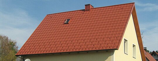 Traditional gable roof with small skylight and chimney, covered with PREFA roof tiles in brick red, including snow guards and roof safety hooks.