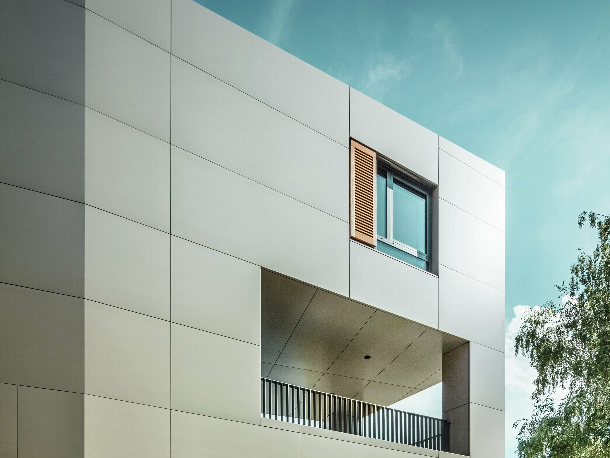 The image shows the modern town hall in Alzenau with a façade made of bronze-coloured aluminium composite panels from PREFA. The architecture is characterised by clear geometric shapes and large windows. The pointed roof and subtle lighting give the building an elegant, contemporary look.