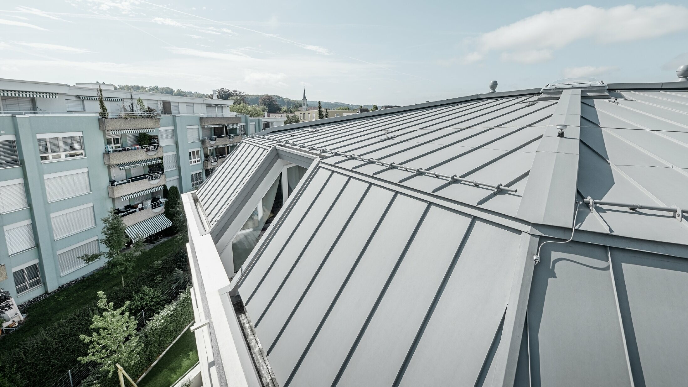 Close up of the roof area of an apartment building. Standing seam roof designed with PREFA Prefalz in patina grey.