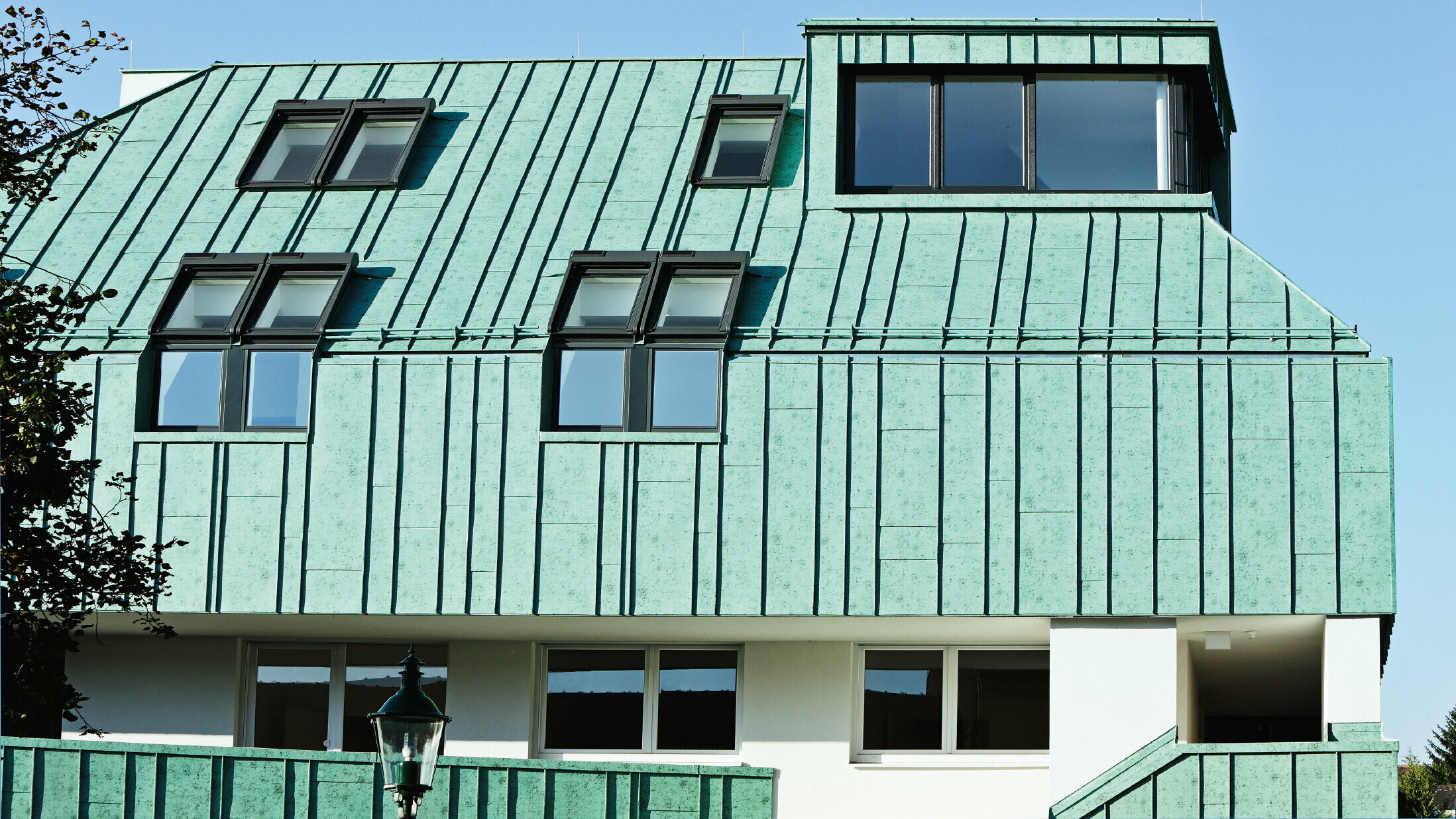 Roof and façade design with PREFALZ standing seam in patina green from PREFA in different panel widths.