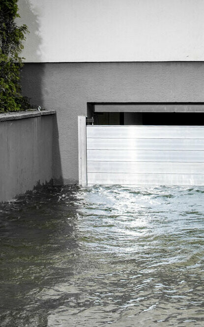 Garageneinfahrt in den Keller mit einem Garagentor das geschützt wird durch den PREFA Hochwasserschutz. Die Einfahrt ist voller Wasser.