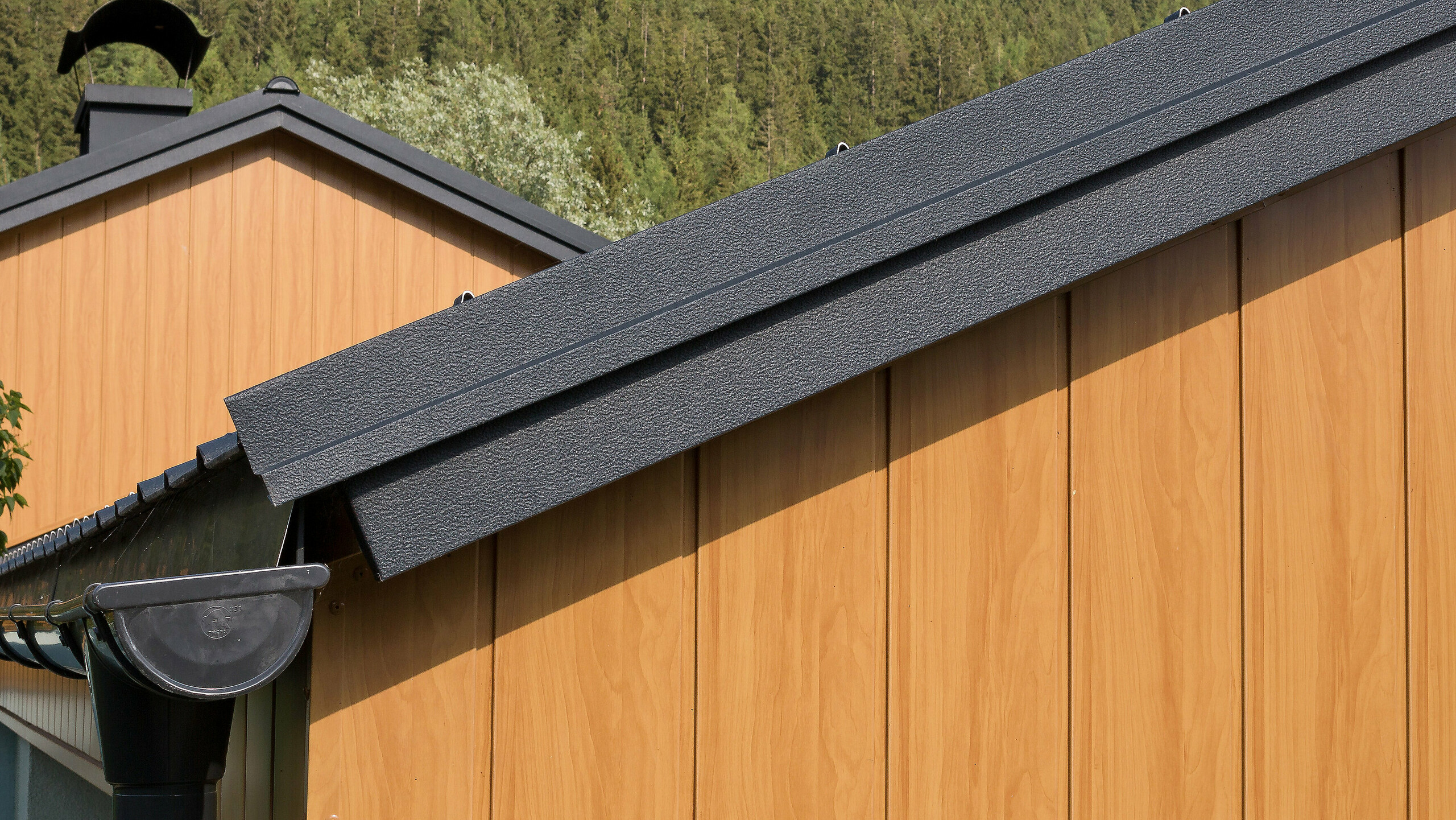 Gable cladding with aluminium sidings from PREFA in natural oak, installed vertically with a PREFA roof gutter in anthracite.