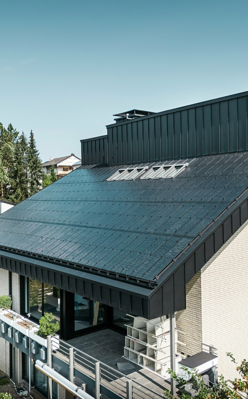 Moderne Architektur eines Einfamilienhauses in Meschede, Deutschland, mit einem PREFALZ-Aluminiumdach in P.10 Schwarz und integrierten Glas/Glas-Photovoltaikmodulen. Das versetzte Dach vereint zeitloses Design mit nachhaltiger Photovoltaik-Technologie. Die innovativen PREFALZ-Solarmodule liefern eine Leistung von 18 kWp. Die rahmenlosen Module und die elegante Aluminium-Dach- und Fassadenverkleidung bilden ein ästhetisches und funktionales Ganzes, das sich harmonisch in die grüne Wohnumgebung einfügt.